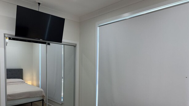 Un dormitorio con cama, televisor montado encima y armario corredero.