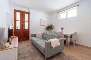 Ein Zimmer mit grauem Sofa, weißem Schreibtisch und Holzboden.