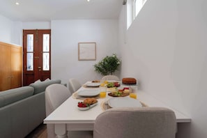 Ein Essbereich mit einem weißen Tisch, der für das Frühstück gedeckt ist, einem grauen Sofa und einer Holztür mit Glasscheiben.