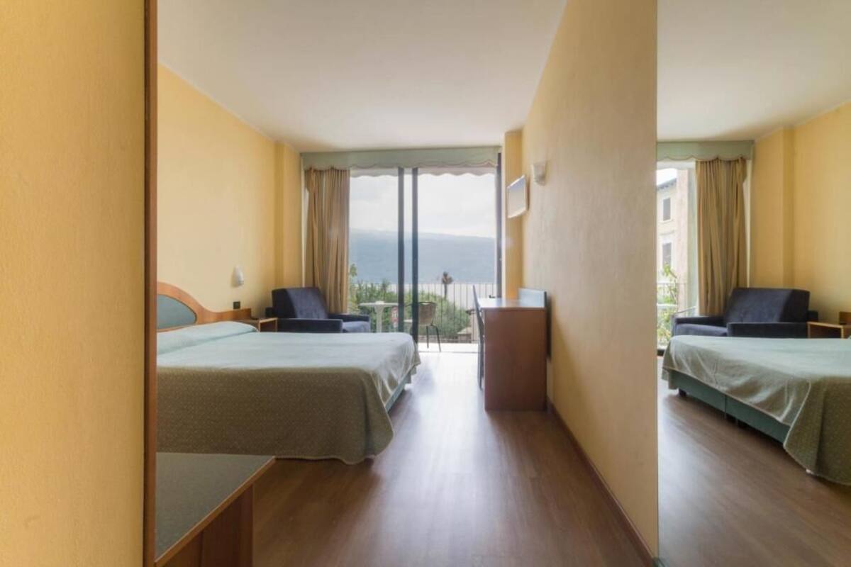 Een hotelkamer met twee bedden, een klein bureau en een balkon met uitzicht op zee.