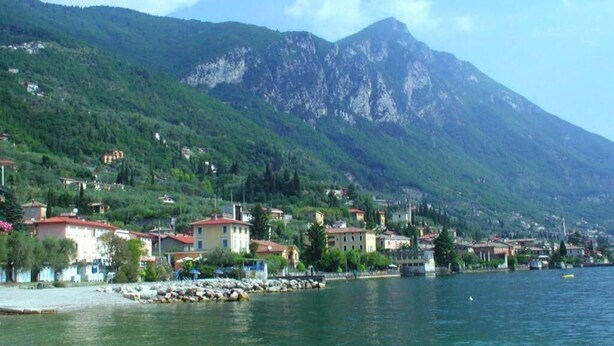 A coastal town with buildings along the waterfront, a clear view of a mountain in the background, and a calm body of water.