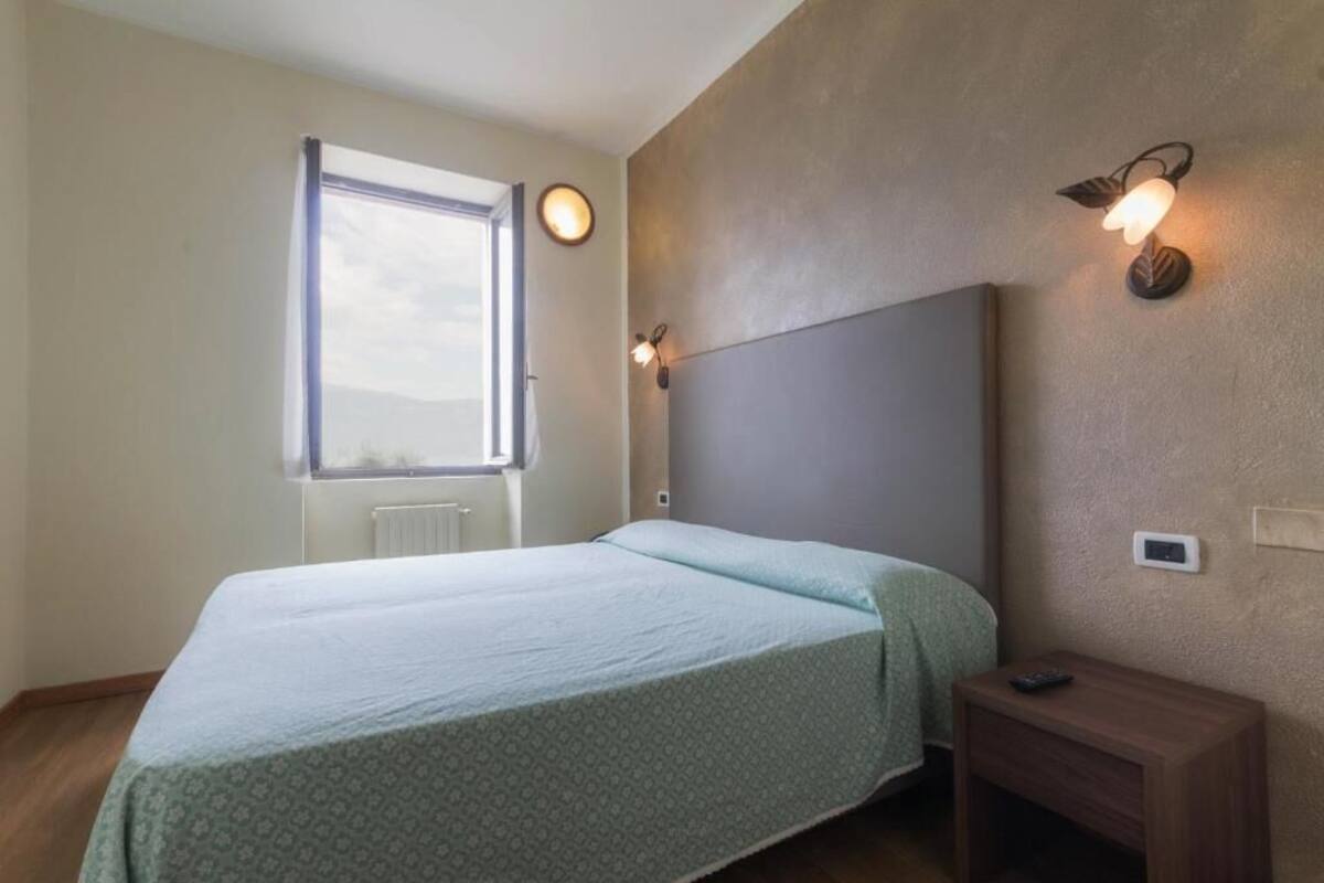 Een slaapkamer met een bed, een nachtkastje, een wandlamp en een raam.