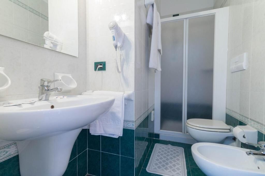 Un baño con lavamanos, inodoro, ducha y un perchero para toallas.