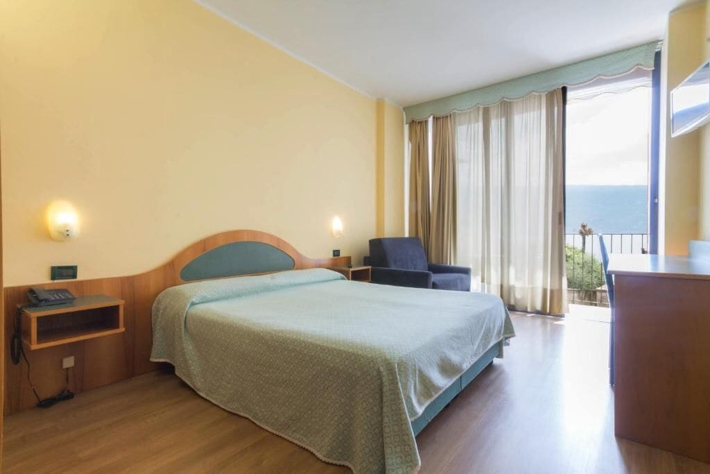 A hotel room with a bed, a desk, a chair, and a balcony with a view.