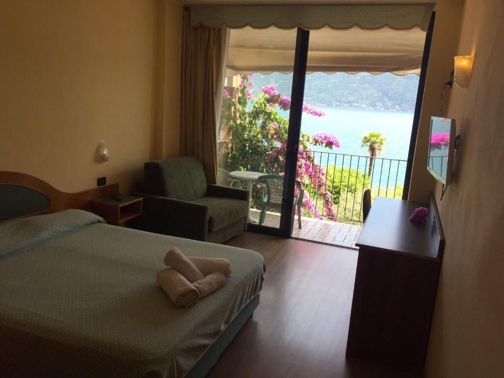 Habitación de hotel con dos camas, un balcón que ofrece vistas a un lago y montañas, una mesita y una silla.