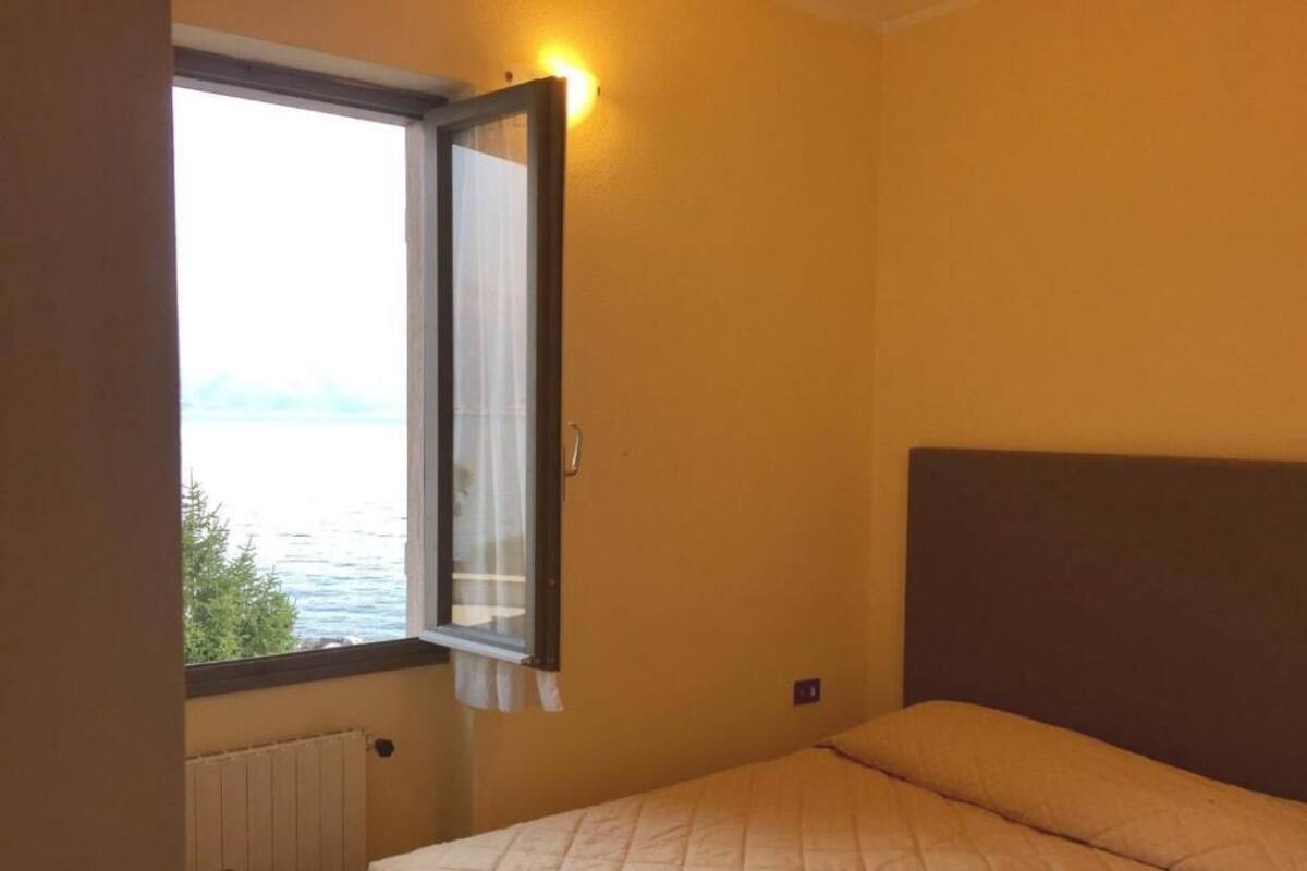 Een slaapkamer met een bed, een raam met gordijnen en uitzicht op zee.