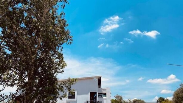 A modern two-story house with a white exterior, a black gate, and a tree in the foreground. - Malkhon Guesthouse (Newcastle)