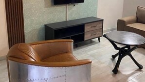 A living room with a sofa, a chair, a TV, and a small table. - Malkhon Guesthouse (Newcastle)