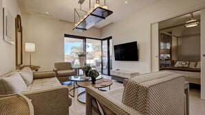 A modern living room with wicker furniture, a flat-screen TV, and a large window offering a view of the outdoors. - Luxury 3 Bed Terraced Apt Near La Cala Beach (La Cala de Mijas)
