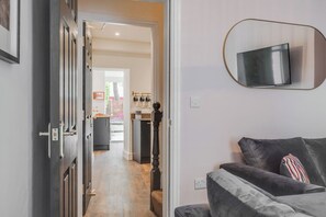 A hallway leading to a kitchen with a dining area, a sofa, and a mounted TV. - The Tides, 3 bed house Morecambe (Lancashire)