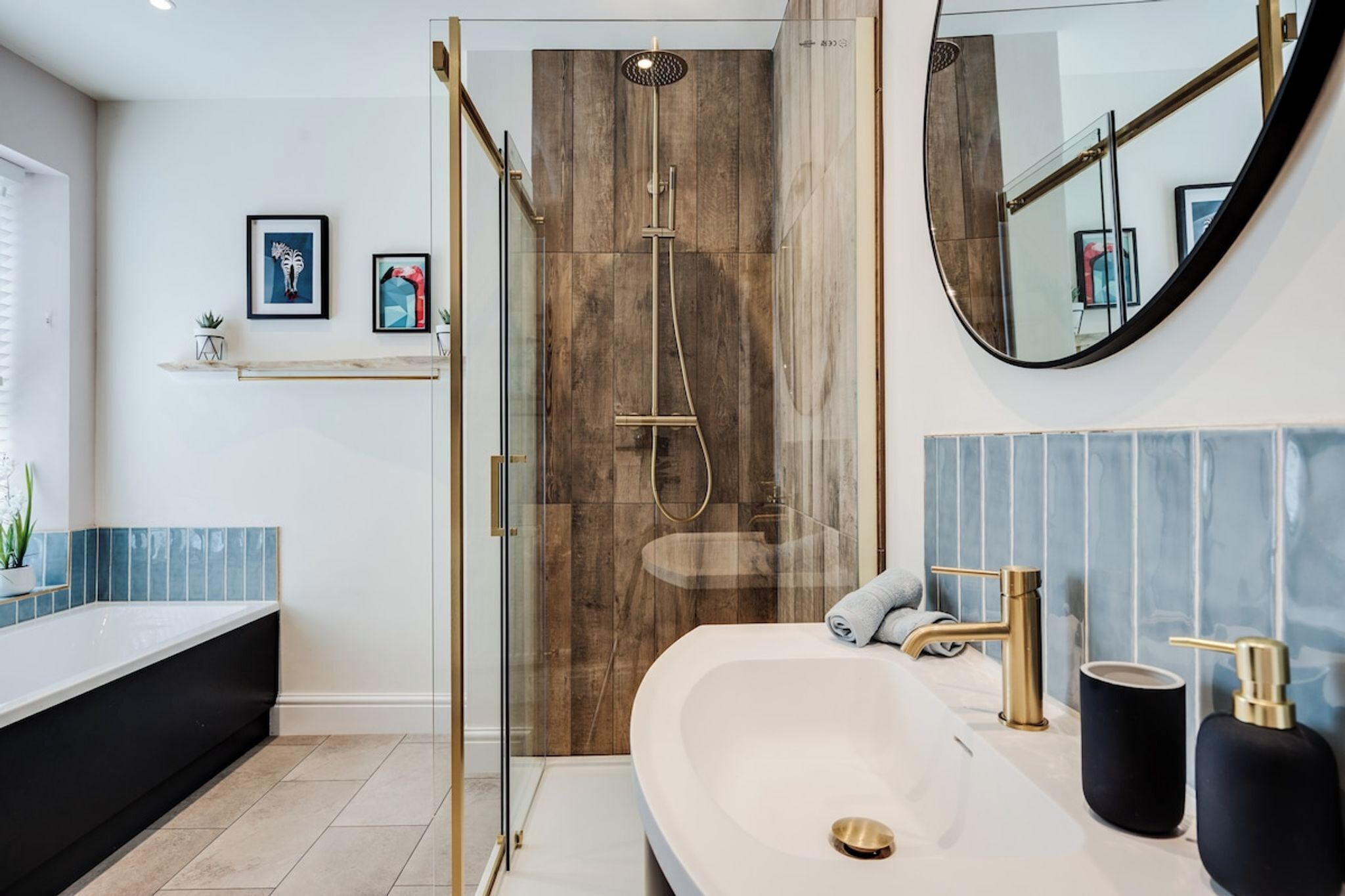 Un baño moderno con ducha de vidrio, un lavamanos grande con detalles dorados y un espejo con marco redondo.