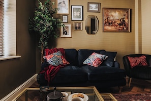 A dark-colored sofa with patterned cushions, a side table with a teapot and cups, and a large mirror on the wall. - Spacious 2 Bed House Lancaster (Lancashire)