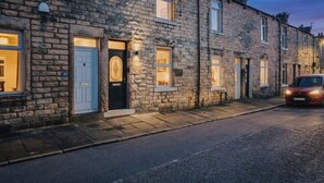 A row of stone buildings with lit windows and a car parked on the street. - Spacious 2 Bed House Lancaster (Lancashire)