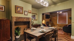 A dining area with a wooden table set for four, a fireplace, and a living room with a sofa and TV. - Spacious 2 Bed House Lancaster (Lancashire)