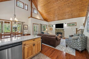 A spacious living area with a fireplace, wooden ceiling, and a stone fireplace. - Forest Ridge Chalet | Tesla EV, Hot Tub (Packwood)
