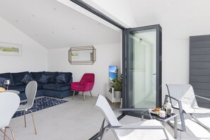 Ein modernes Wohnzimmer mit einer Couch, Sesseln, einem Esstisch und einem Balkon mit Glastür.