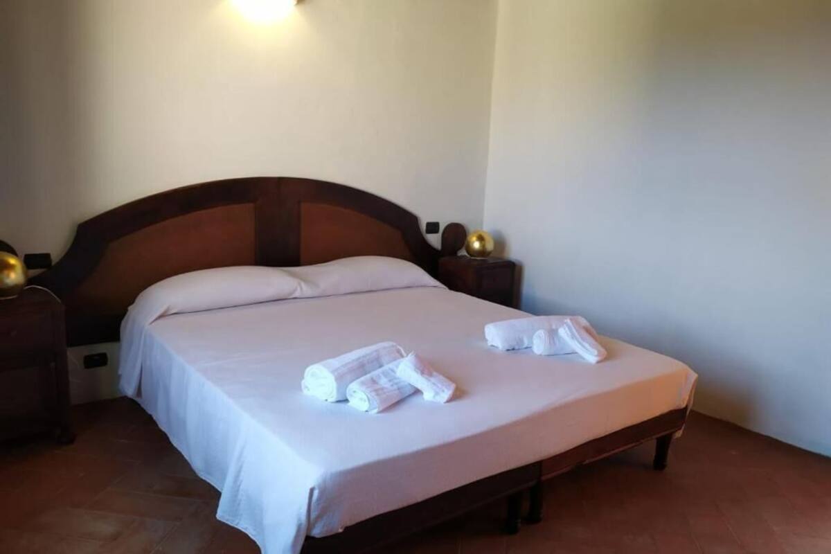 Una cama doble con ropa de cama blanca, dos mesitas de noche con lámparas y un aplique en la pared.
