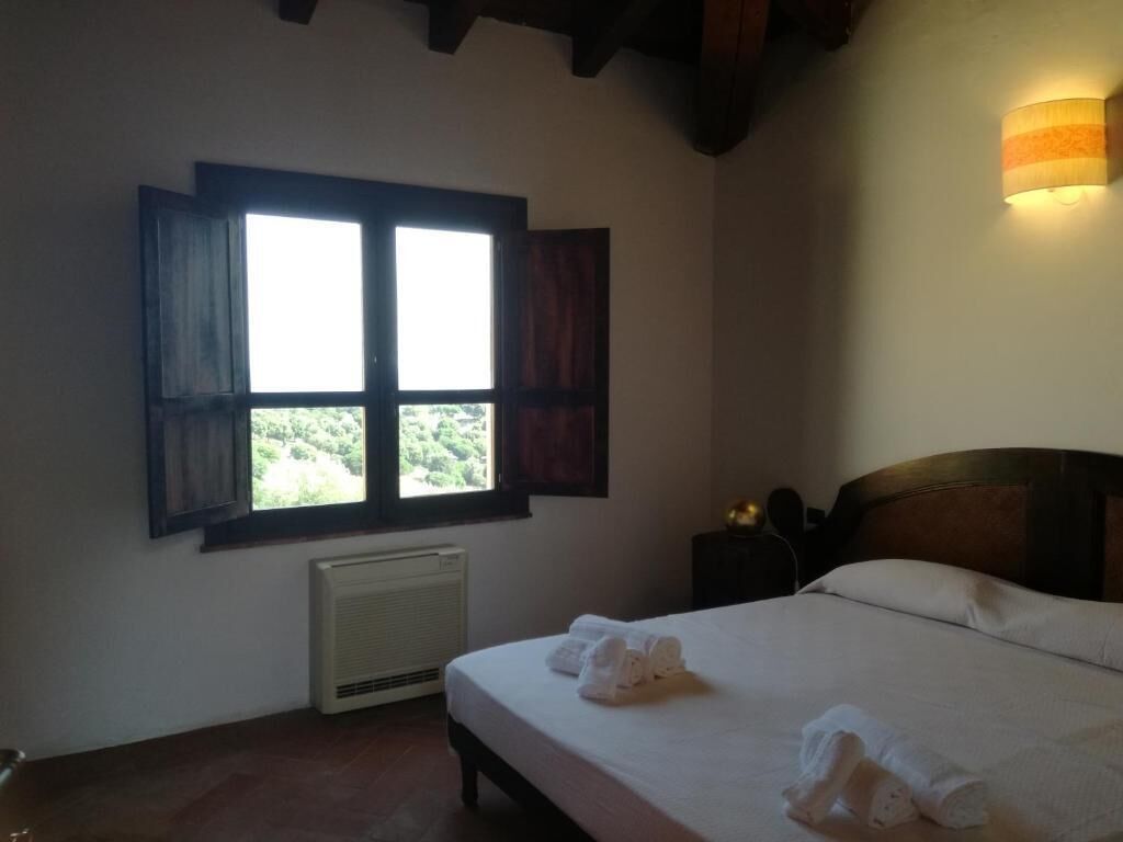 A bedroom with a bed, a window with shutters, a radiator, and a wall-mounted light fixture.