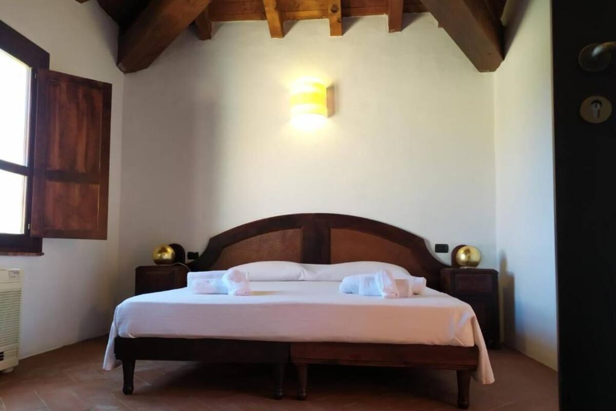 Un dormitorio con una cama de madera, una mesita de noche con una lámpara, un radiador y una ventana con marco de madera.