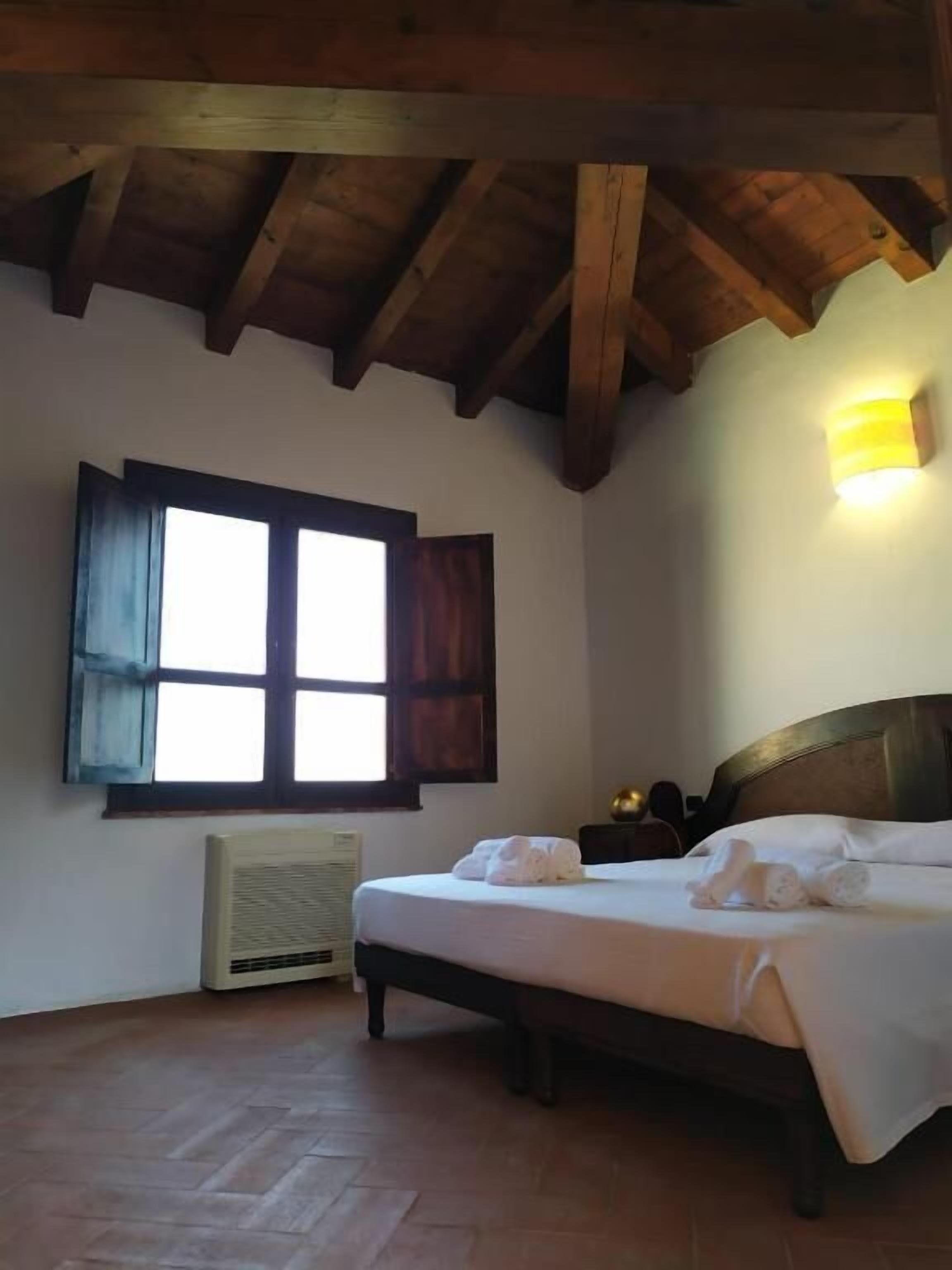 A bedroom with a bed, a window with shutters, a wall-mounted light, and a radiator.