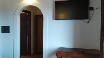 Ein Zimmer mit Holzboden, einem Wand-Fernseher, einem Holztisch und Fliesenboden.