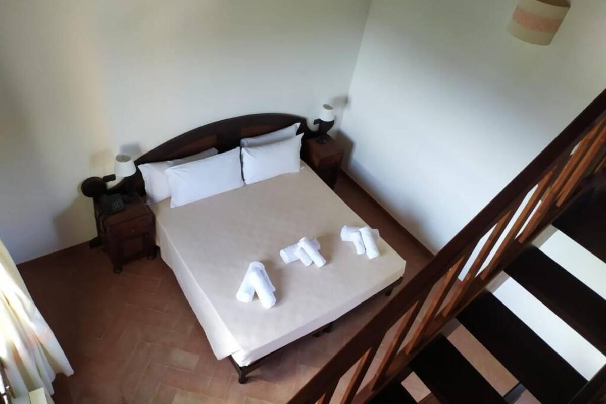 Un dormitorio con cama, mesitas de noche, una silla de madera y una escalera.