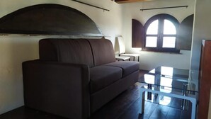A room with a dark-colored sofa, a glass coffee table, and a window with a view.