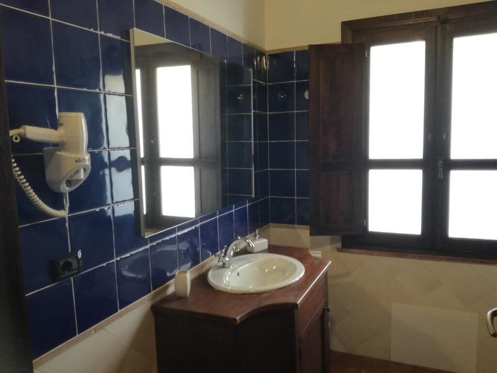 A bathroom with blue tiles, a white sink, a mirror, and a window.