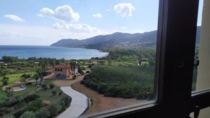 A coastal landscape with a winding road, a building, and a view of the sea and mountains.
