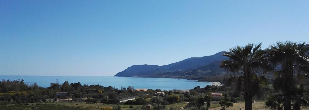 Eine Küstenlandschaft mit blauem Himmel, Wasser und einem Berg im Hintergrund.