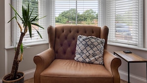 Une pièce d’angle avec un fauteuil en cuir marron, un coussin décoratif à motifs, une petite table et une plante en pot.