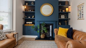 Un salon avec une cheminée bleue, un miroir rond et une bibliothèque contenant divers objets décoratifs.