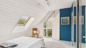 Un dormitorio con tragaluz, una cama, una silla y una pared azul decorativa.
