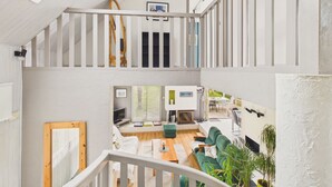 Un interior de varios niveles con una escalera, un comedor y una sala de estar con sofá y televisor.