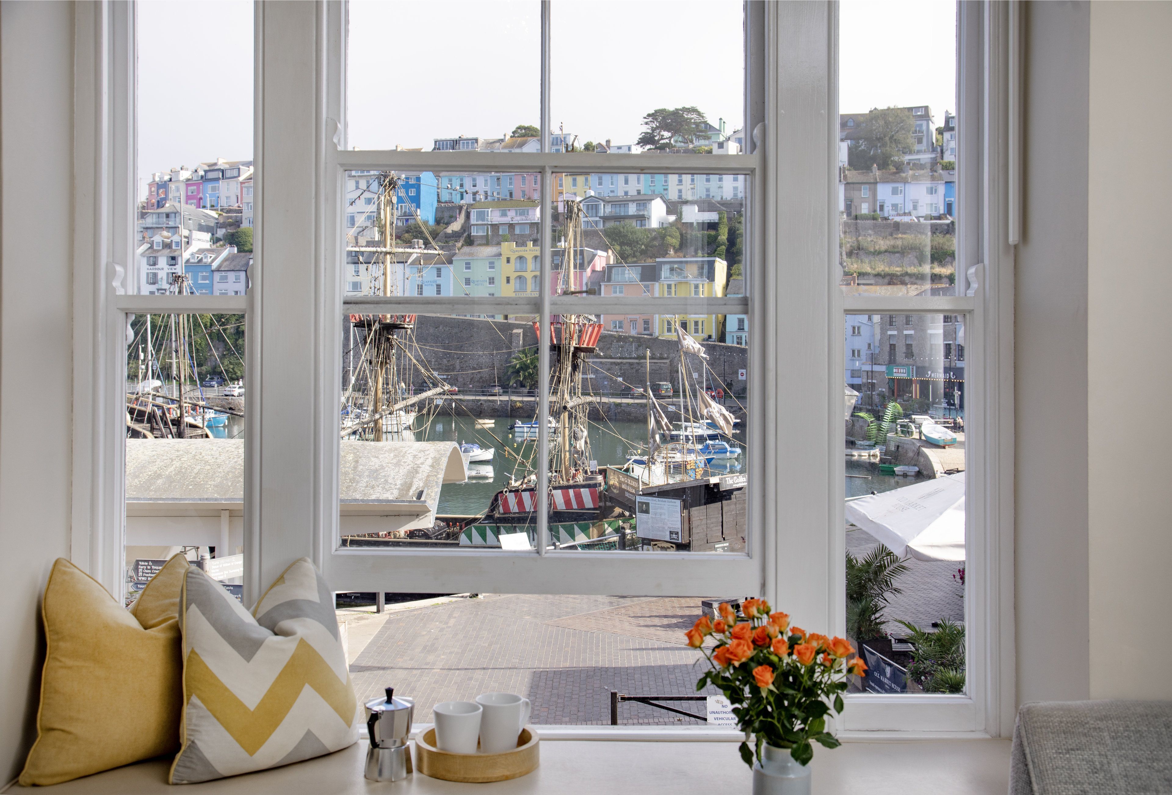 Una finestra con vista su un porto, edifici colorati e un cartello con la scritta 'The Golden Mermaid'.