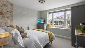 Ein Schlafzimmer mit einem Bett, einem Fernseher, einem Fenster mit Blick auf Gebäude und einer Pflanze auf einer Kommode.
