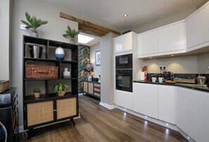 A modern kitchen with white cabinets, a built-in oven, and a black island with a sink. - Seven - La Petite Maison is a stylish, dog-friendly holiday home in Brixham (Brixham)