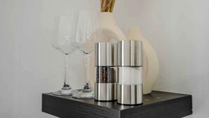 Uma prateleira preta com três recipientes metálicos e duas taças de vidro.