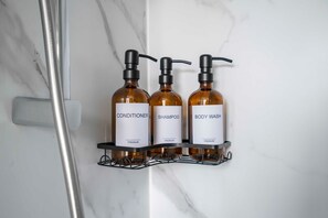 Et badeværelse med marmorvæg, brusebad og tre toiletartikler på en hylde.
