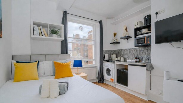 Quarto moderno com uma cama grande, máquina de lavar e cozinha equipada com TV e micro-ondas.