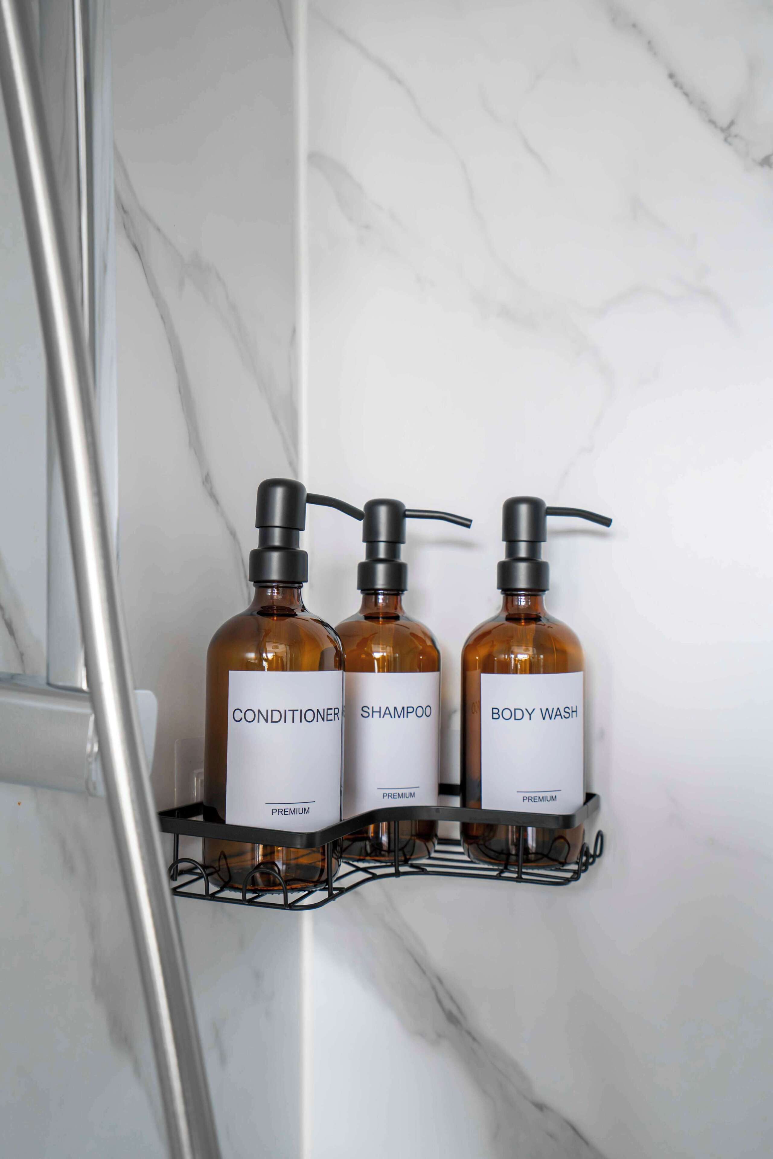 Drie flessen luxe persoonlijke verzorgingsproducten op een metalen rek voor een marmeren wand.