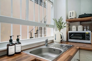 A kitchen with a stainless steel sink, a white toaster, a white microwave, and two bottles of dish soap. - West Kensington Mezzanine Studio | 3-Min Tube | Sleeps 3 (Greater London)