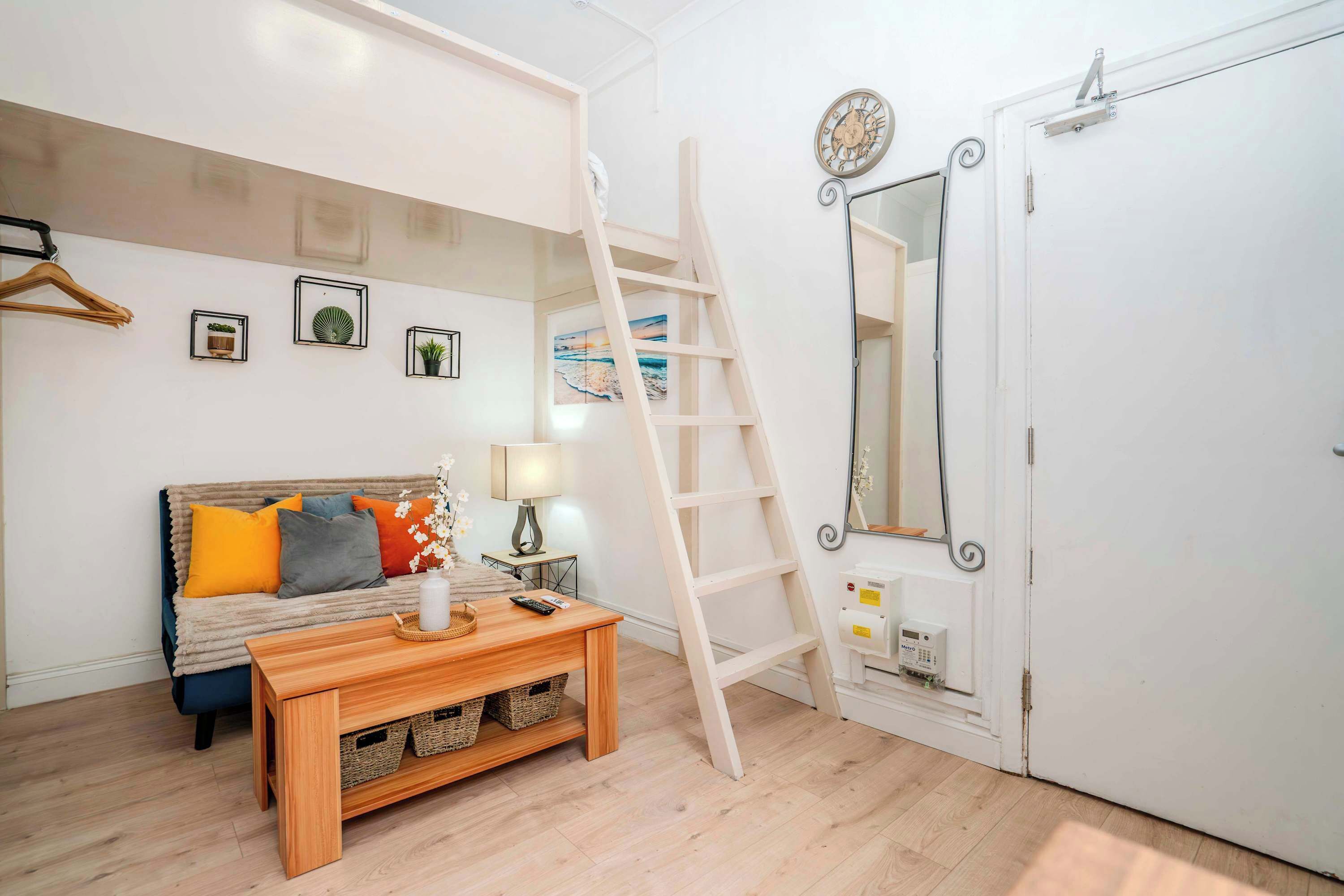 Een kamer met een bed, een houten tafel, een ladder, een spiegel en ingelijste foto's aan de muur.