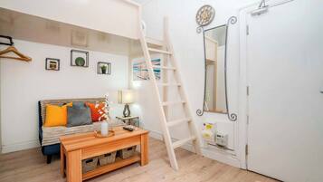 Een kamer met een bed, een houten tafel, een ladder, een spiegel en ingelijste foto's aan de muur.