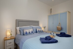 A bedroom with a bed, bedside tables, a wardrobe, and a nightstand. - Old Mill Court is a charming, dog-friendly two-bedroom cottage in Brixham (Brixham)