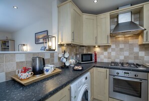 A modern kitchen with a gas stove, microwave, kettle, and a built-in washing machine. - Old Mill Court is a charming, dog-friendly two-bedroom cottage in Brixham (Brixham)