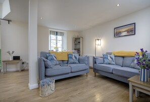 A modern living room with two grey sofas, a small table, and a wall-mounted picture. - Old Mill Court is a charming, dog-friendly two-bedroom cottage in Brixham (Brixham)