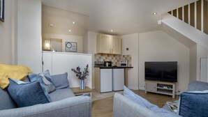 Een moderne woonkamer met een grijze zithoek, een flatscreen televisie en een keuken met een inbouwoven en magnetron.