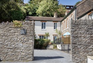 A stone-walled courtyard with a white building, a gate, and a blue umbrella. - Old Mill Court is a charming, dog-friendly two-bedroom cottage in Brixham (Brixham)