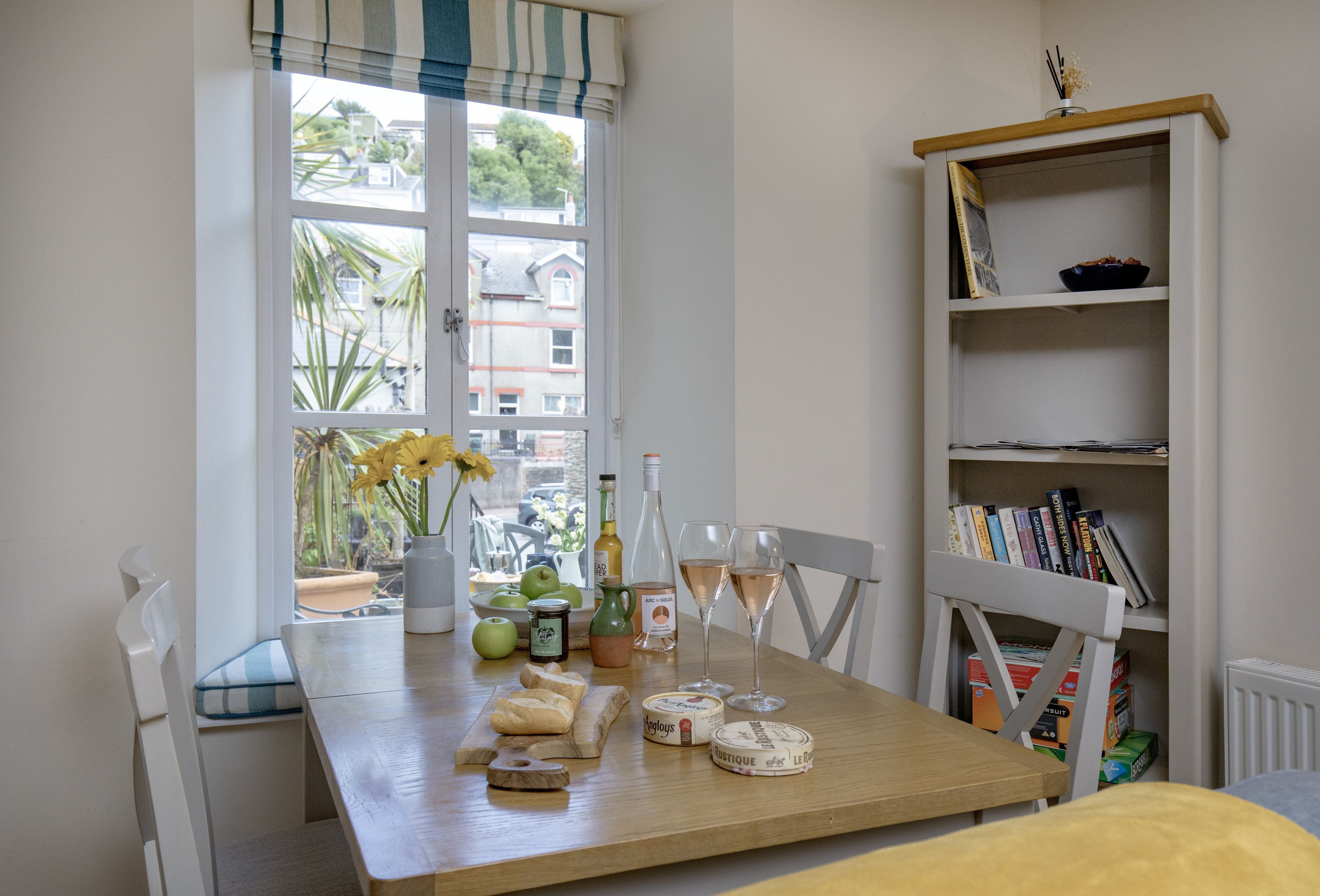 A dining table with a view of the outside, a bookshelf, and various food items.